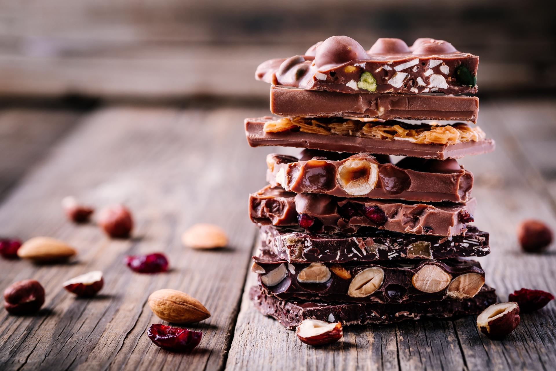 Stack of  milk and dark chocolate with nuts, caramel and fruits and berries on wooden background.