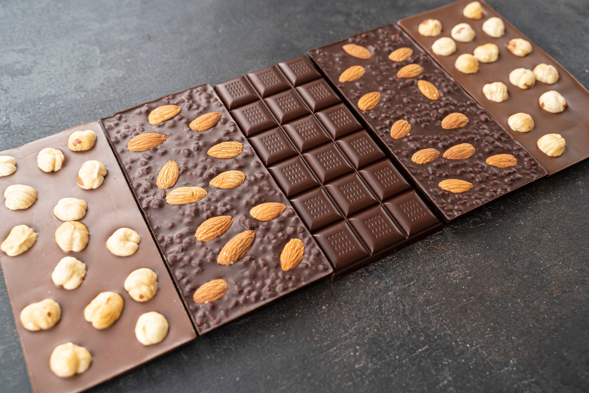 assortment chocolate bars with almonds, hazelnuts, handmade sweets. Composition of bars milk and dark almond chocolates hazelnuts on a black background, top view. Pastry craft on the table for chocolate background